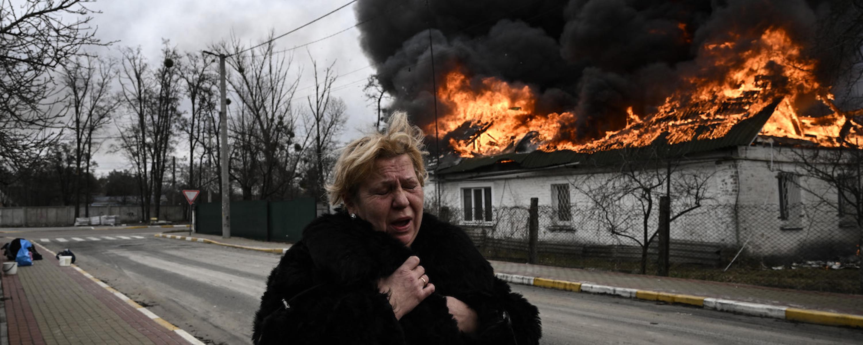 Eine trauernde Frau steht vor einem brennenden Wohngebäude.