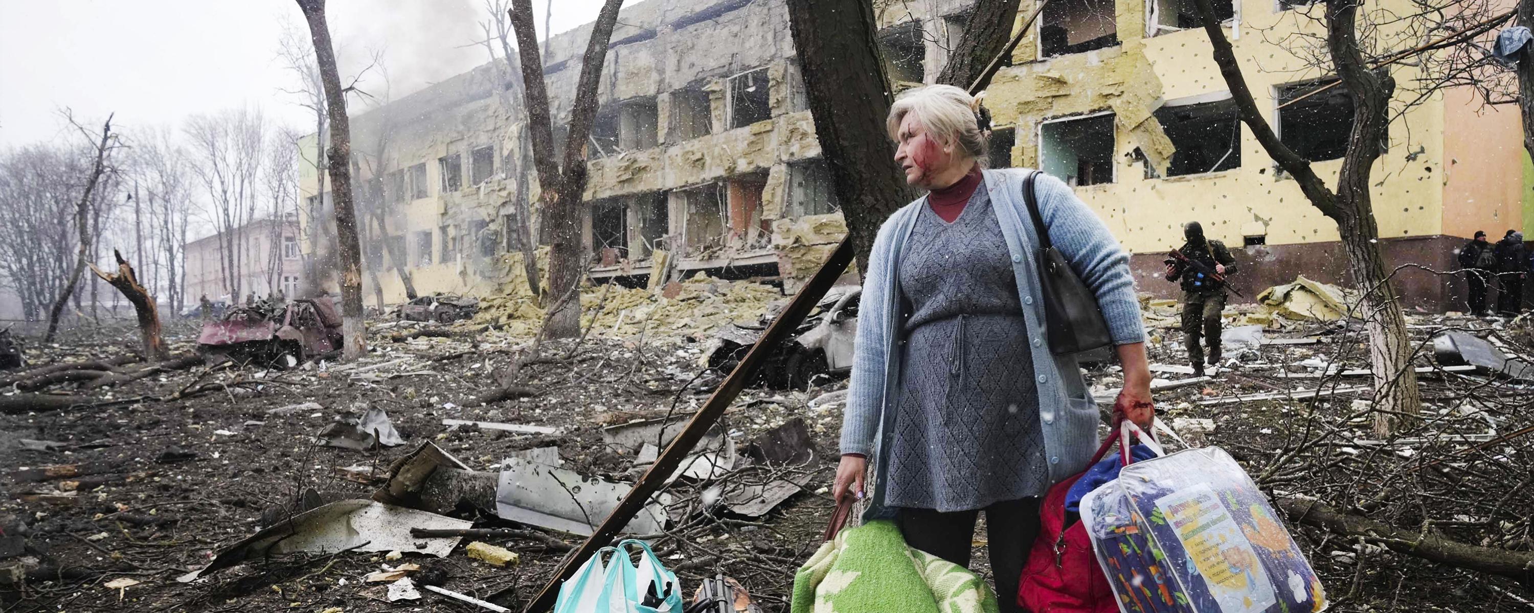 Eine Frau mit Taschen in der Hand verlässt ihr zerstörtes Wohngebäude.