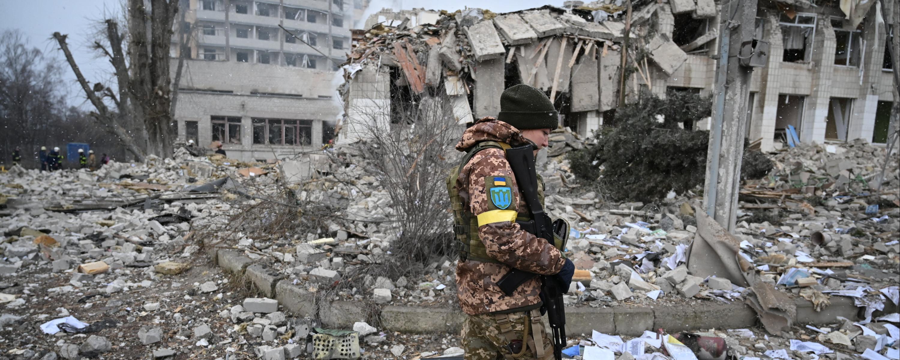 Eine ukrainische Soldatin läuft mit gesenktem Blick und Waffe in der Hand über ein Trümmerfeld.
